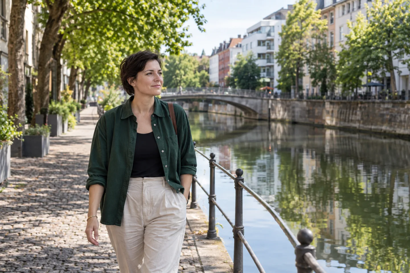 Eine Frau in grünem Hemd geht bei Tageslicht an einem städtischen Kanal entlang.
