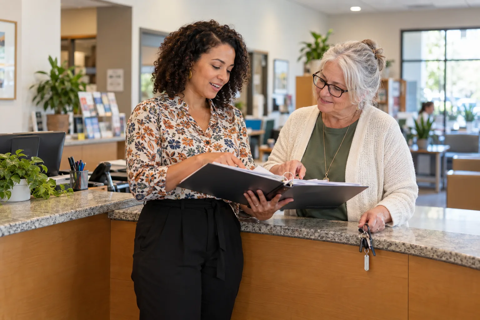 Two women review a binder together at a reception counter.